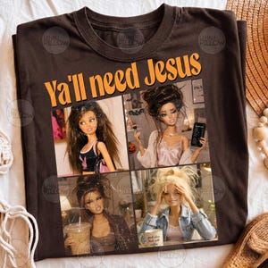 May include: A dark brown t-shirt featuring the orange text "YA'll need Jesus" above a collage of four images of dolls. The dolls are depicted in various settings, including holding a coffee cup, applying makeup, and wearing casual clothing.