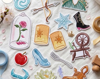 May include: A collection of embroidered patches featuring various icons including a rose in a glass dome, a bow and arrow, a spinning wheel, a magic lamp, a glass slipper, a red apple, a lotus flower, a snowflake, and a sun lantern.