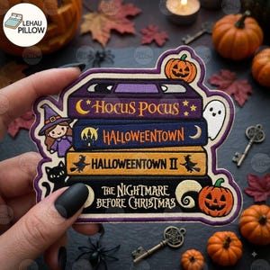 Könnte beinhalten: Ein bestickter Aufnäher mit einem Stapel aus vier VHS-Kassetten mit den Titeln Hocus Pocus, Halloweentown, Halloweentown II und The Nightmare Before Christmas. Das Design zeigt eine kleine Hexe, eine schwarze Katze, ein Gespenst und zwei Kürbisse.