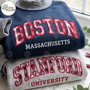 May include: A navy blue sweatshirt with a mock neck featuring a red and white gingham pattern, displaying the embroidered text BOSTON MASSACHUSETTS, stacked above a grey sweatshirt with STANFORD UNIVERSITY text and a black and white gingham pattern.
