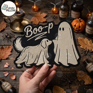 May include: A black embroidered patch featuring a beige ghost and a dog wearing a ghost costume. The text Boo-p is stitched in beige above the figures. The design is shaped with a black border and depicts a playful Halloween-themed scene.