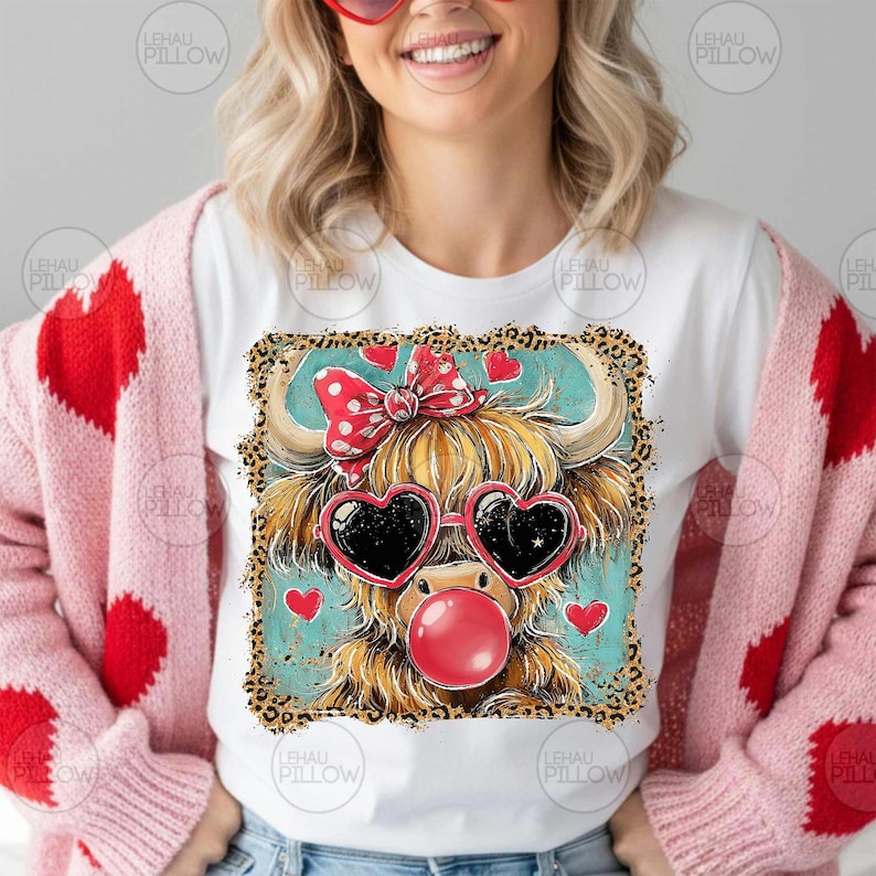 Peut inclure: T-shirt blanc avec une vache des Highlands de dessin anim&eacute; portant des lunettes de soleil en forme de c&oelig;ur et une bulle de chewing-gum. La vache a un n&oelig;ud rouge et est entour&eacute;e de c&oelig;urs. Th&egrave;me de la Saint-Valentin.
