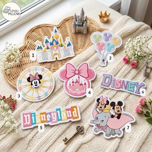 May include: A collection of seven embroidered patches featuring Disney themes, including a castle, Mickey-shaped balloons, a Ferris wheel with Minnie Mouse, a Disneyland logo, the word Disney, and Dumbo with Mickey Mouse, all arranged on a textured surface.