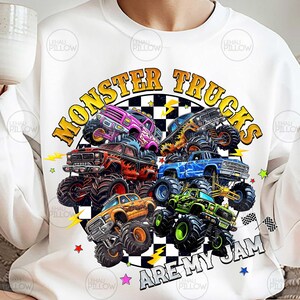 Peut inclure: Sweat-shirt blanc avec un motif color&eacute; de monster trucks de diff&eacute;rentes couleurs, dont rose, orange, bleu et vert. Le texte "MONSTER TRUCKS ARE MY JAM" est affich&eacute; dans un cercle avec des &eacute;clairs et des &eacute;toiles.