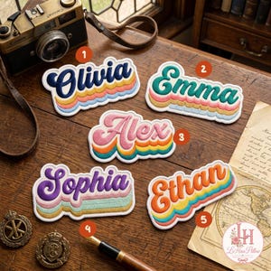 May include: Five embroidered name patches featuring the names Olivia, Emma, Alex, Sophia, and Ethan in a retro, multi-layered, wavy font style. Each patch displays a unique colour combination with a white border, arranged on a wooden surface.