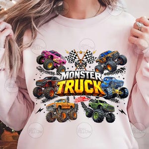 Może przedstawiać: Jasnor&oacute;żowa bluza z kolorową grafiką przedstawiającą kilka monster truck&oacute;w w r&oacute;żnych kolorach, w tym r&oacute;żowym, pomarańczowym, niebieskim i zielonym. Tekst "MONSTER TRUCK" jest wyraźnie wyświetlany na środku, z szachownicami i gwiazdami.