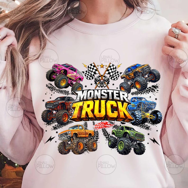 Może przedstawiać: Jasnor&oacute;żowa bluza z kolorową grafiką przedstawiającą kilka monster truck&oacute;w w r&oacute;żnych kolorach, w tym r&oacute;żowym, pomarańczowym, niebieskim i zielonym. Tekst "MONSTER TRUCK" jest wyraźnie wyświetlany na środku, z szachownicami i gwiazdami.
