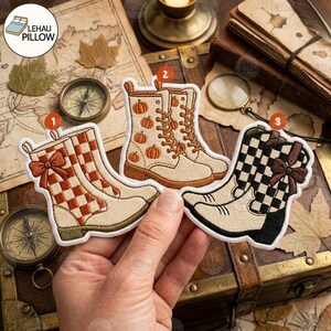 Peut inclure: Trois écussons thermocollants brodés en forme de bottes. Le numéro 1 est une botte crème à motif damier orange avec un nœud. Le numéro 2 est une botte crème avec des citrouilles orange. Le numéro 3 est une botte crème à damier noir avec un nœud.