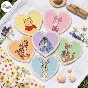 May include: Six heart-shaped fabric coasters featuring embroidered illustrations of Winnie the Pooh, Piglet, Eeyore, Tigger, Kanga with Roo, and Rabbit. Each coaster has a scalloped cream-colored border and a unique pastel-colored background.