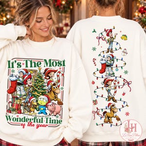 May include: A cream-colored crewneck sweatshirt featuring Toy Story characters in Christmas attire. The front displays the text It's The Most Wonderful Time of the year with Woody, Buzz, and friends near a tree. The back shows a string of lights.