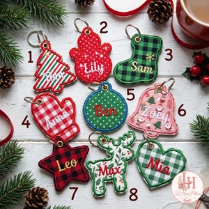 May include: Eight embroidered Christmas ornaments with metal keyrings, each featuring a unique shape and name: Tom on a striped tree, Lily on a red snowman, Sam on a green plaid stocking, Anna on a red gingham mitten, Ben on a green polka dot circle, Zoey on a bell, Leo on a red and black plaid star, Max on a reindeer, and Mia on a green plaid heart.