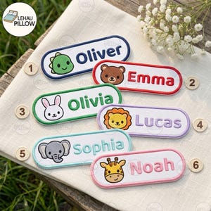 May include: Six oval embroidered name patches featuring cartoon animal faces and names. The patches include a green dinosaur labelled Oliver, a brown bear labelled Emma, a white rabbit labelled Olivia, a yellow lion labelled Lucas, a grey elephant labelled Sophia, and a yellow giraffe labelled Noah.