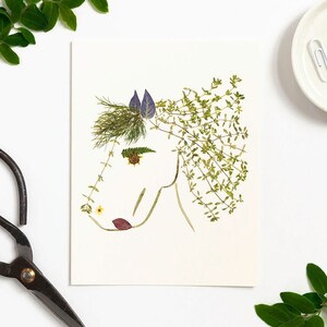 May include: A white card with a horse silhouette made from pressed flowers and leaves. The horse has a purple flower for an ear, green leaves for its mane, and a yellow flower for an eye.