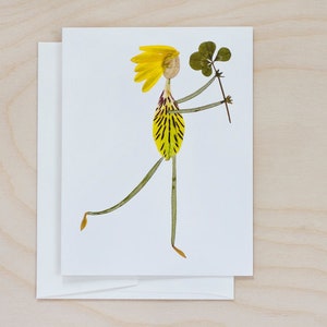 May include: A whimsical greeting card featuring a person made of pressed flowers. The person is holding a four-leaf clover and has yellow hair and a yellow and green dress.