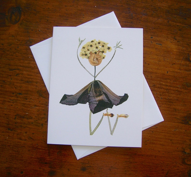 May include: A greeting card featuring a whimsical flower arrangement that resembles a person. The person is made of dried flowers and has a dark purple skirt, yellow flower hair, and green stems for arms and legs.