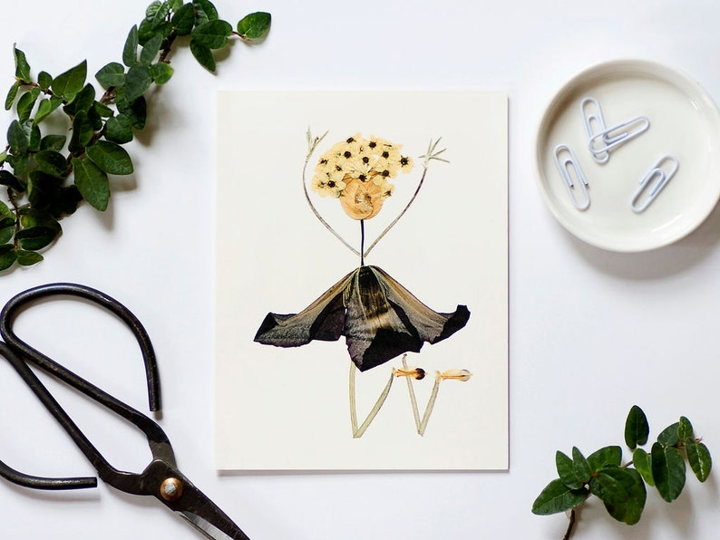 May include: A greeting card featuring a whimsical flower person made from pressed flowers. The person has a yellow flower head, a black flower skirt, and long, thin stems for arms and legs.