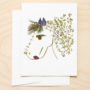 May include: A white card with a horse's head made from pressed flowers and leaves. The horse's mane is made from green leaves, the ears are purple, and the nose is a yellow flower.