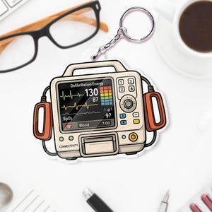 May include: A keychain featuring a cartoon-style defibrillator with a screen displaying vital signs. The screen shows a heart rate of 130, SpO2, and other readings. The keychain has a silver chain and a handle.