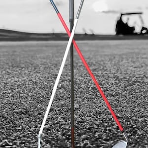 Puede incluir: Tres palos de golf con empuñaduras y cabezas de palo de diferentes colores. Los palos están en un campo de golf verde con un carro de golf en el fondo.