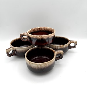 May include: Four ceramic soup bowls with handles. The bowls are a deep brown color with a lighter brown and cream-colored rim. The handles have a circular opening. The bowls are stacked in a slightly offset arrangement against a white background.
