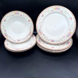 May include: A set of white ceramic dinnerware with a floral design. The plates and bowls have a light pink border with a floral pattern in shades of pink, yellow, and purple. The set includes both plates and bowls.