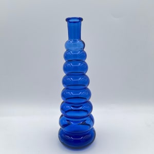 May include: A tall, cobalt blue glass vase with a unique, stacked bubble design. The vase has a narrow neck and a wide, rounded base. The body of the vase is composed of several rounded sections, creating a textured appearance. The vase is approximately 12 inches tall.