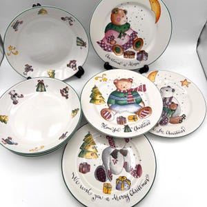 May include: A set of five white ceramic plates with green rims, featuring illustrations of teddy bears, Christmas trees, and wrapped gifts. Text on the plates includes "Christmas is Magic," "Home for Christmas," and "We wish you a Merry Christmas."