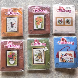 May include: Six Jiffy Stitchery embroidery kits in plastic packaging. Designs include a mouse with text, yellow daffodils, two harvest scenes, colorful tulips, a country house, and a wall hanging with the text Diane's Room and red tassels.