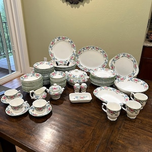 May include: A collection of vintage china with a floral pattern. The set includes plates, bowls, cups, saucers, a teapot, a creamer, a sugar bowl, serving dishes, and salt and pepper shakers. The china features a white background with a pink and blue floral design.