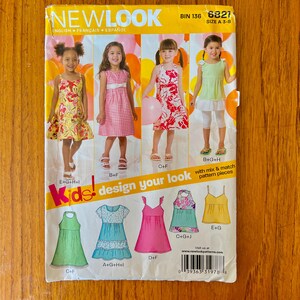 May include: A New Look sewing pattern envelope for children's clothing, labeled BIN 136 and 6821, size A 3-8. The front displays three children wearing various sleeveless dresses and tops, with illustrations of garment designs and a barcode at the bottom.
