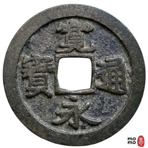 Puede incluir: Una taza de cerámica blanca con un asa negra y el texto "But First, Coffee" en negrita negra. La taza está sobre un fondo borroso. La taza mide aproximadamente 10 cm de altura.