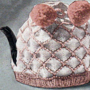 Può includere: Una coperta per teiera lavorata a maglia con un motivo a rombi e due grandi pompon rotondi rosa sulla parte superiore. La coperta è principalmente bianca con cuciture rosa e una base marrone. Il manico e il beccuccio sono neri.