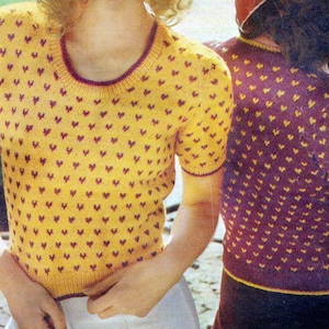 Può includere: Due top in maglia a maniche corte. Uno è giallo con cuori bordeaux, l'altro è viola con cuori gialli. Entrambi hanno uno scollo tondo e sono probabilmente fatti a mano. I top sono in stile vintage.