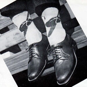 May include: Black leather dress shoes with a lace-up design. The shoes are paired with argyle socks in shades of white, gray, and black. The image is a close-up shot of the shoes and socks.