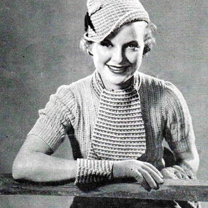 Pode incluir: Uma mulher vestindo um chapéu de malha e um suéter e luvas combinando. O chapéu é de estilo folgado com uma aba e um pequeno laço. O suéter tem uma gola alta e um padrão de nervuras. As luvas são sem dedos e têm um padrão de nervuras.