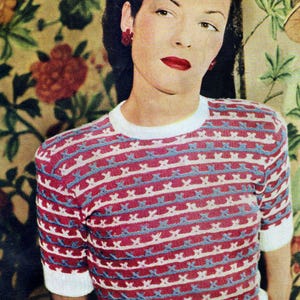May include: A vintage-style short-sleeved top with a red and white striped pattern, accented with blue details. The top has a white collar and cuffs. The person in the image is wearing red earrings and red lipstick.