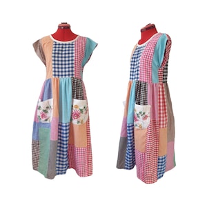 Könnte beinhalten: Ein Patchwork-Kleid mit rundem Ausschnitt und kurzen Ärmeln. Das Kleid weist eine Vielzahl von Vichy-Mustern in Farben wie Rosa, Blau und Orange auf. Zwei Taschen mit floralen Stickereien sind auf der Vorderseite sichtbar. Das Kleid wird auf einer roten Schneiderpuppe präsentiert.