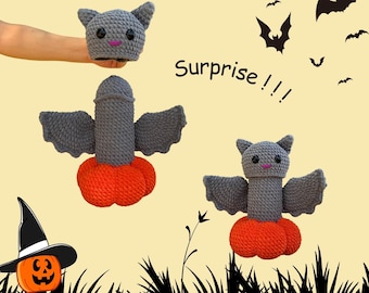May include: A crocheted bat toy with a grey body, orange base, and bat wings. The toy has a bat head with small ears and a pink mouth. The image includes the text "Surprise!!!" and a jack-o'-lantern.