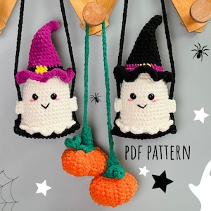 Puede incluir: Dos bolsas de Halloween de crochet en forma de fantasma con correas negras y sombreros de bruja. Un fantasma tiene un sombrero rosa y el otro un sombrero negro. Las bolsas están colgadas de ganchos y hay calabazas y estrellas en el fondo.  PDF PATTERN