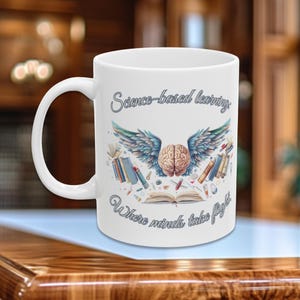 May include: White ceramic mug with a blue and brown illustration of a brain with wings and books. The text "Science-based learning. Where minds take flight." is printed on the mug.