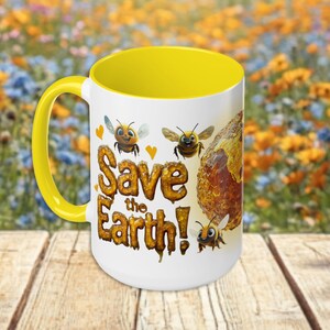 May include: White ceramic mug with a yellow rim. The mug features a cartoon illustration of bees and honeycomb with the text "Save the Earth!" in dripping honey letters.