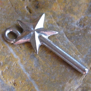 May include: Silver charm in the shape of a star-topped wand. The wand has a loop at the top for attaching to a bracelet or necklace.