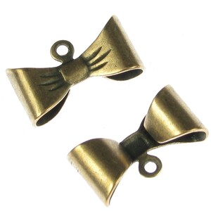 May include: Two antique gold-toned metal bow-shaped clasps with a loop at the top.