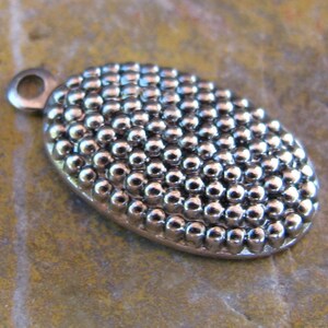 May include: Silver oval charm with a textured surface of small, raised dots.