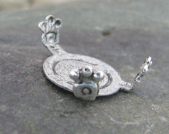 Puede incluir: Encanto de plata con un diseño redondo texturizado y un detalle de huella de pata. El encanto tiene dos bucles para sujetarlo a una pulsera o collar.