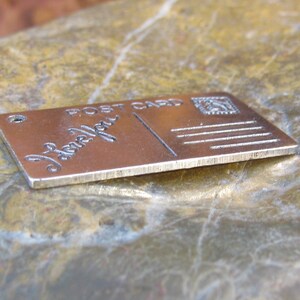 May include: A silver metal charm shaped like a postcard with the words "Post Card" and "Love You" engraved on it.