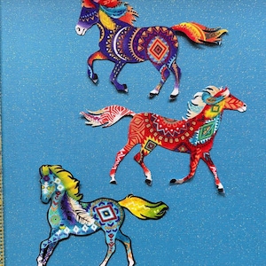 May include: Three colorful horse appliques with geometric patterns in shades of red, blue, yellow, and white. The horses are on a blue background.