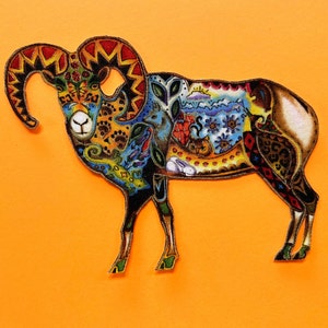 May include: A colorful ram patch with intricate patterns and designs. The ram features a mix of colors, including blue, yellow, red, and brown, with detailed artwork inside its body. The patch is set against an orange background.