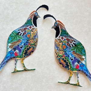 May include: Two colorful quail fabric appliques. Each bird features a black crest, a black and white face, and a body adorned with a vibrant mix of patterns, including leaves, animals, and geometric shapes. The birds stand on green and yellow legs.