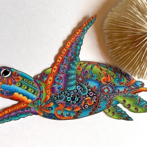 May include: A colorful, intricately patterned wooden turtle sculpture with a blue, green, orange, and purple design. The turtle is in a flying position with its head and flippers extended.
